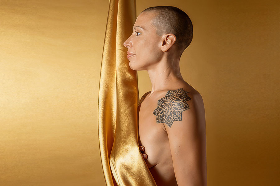 Woman recovering from breast cancer treatment, photographed in profile against gold silk