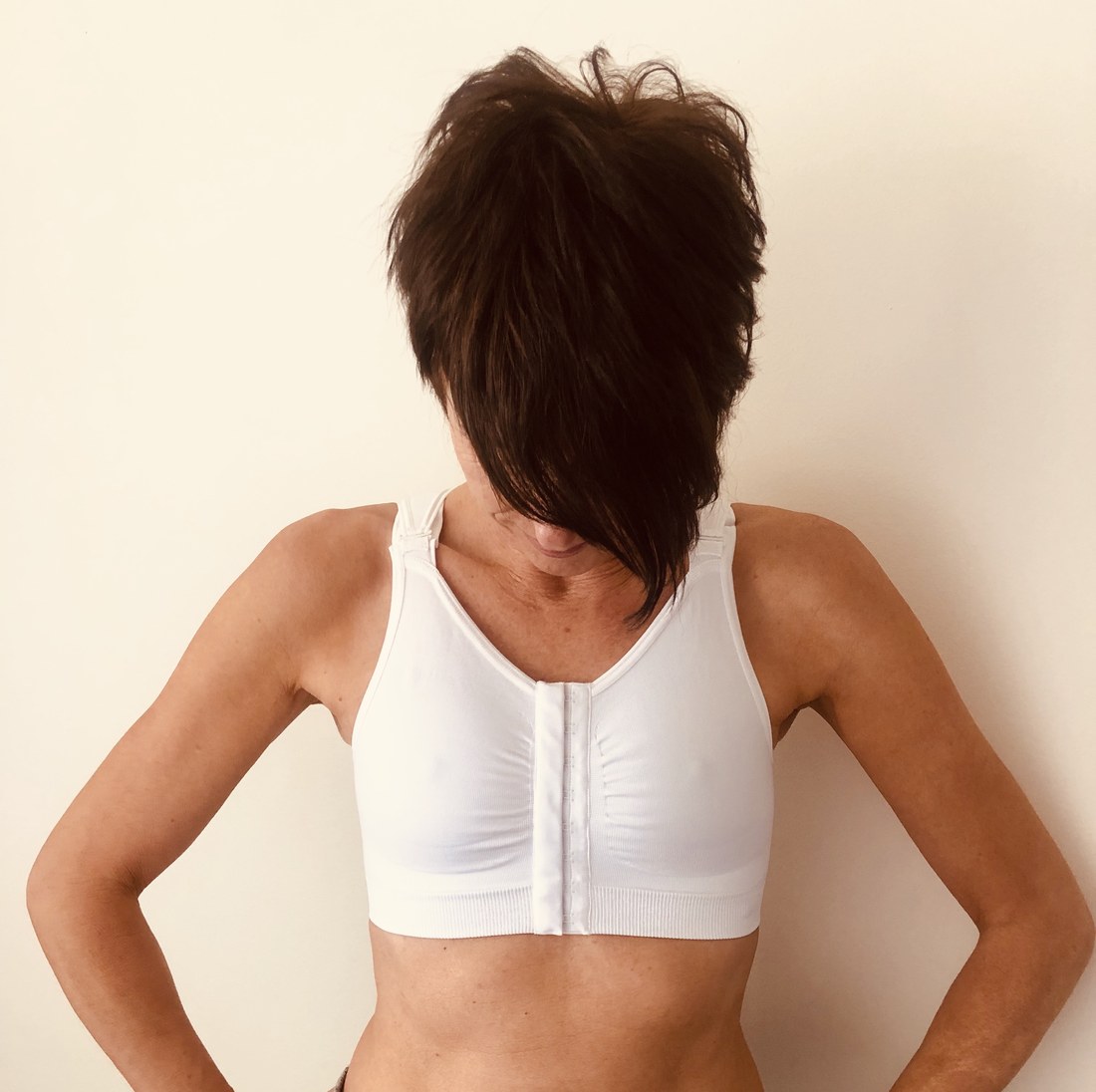 Woman wearing the white Reco Bra with her head lowered, showing how the fabric moulds to the chest after breast implant removal surgery