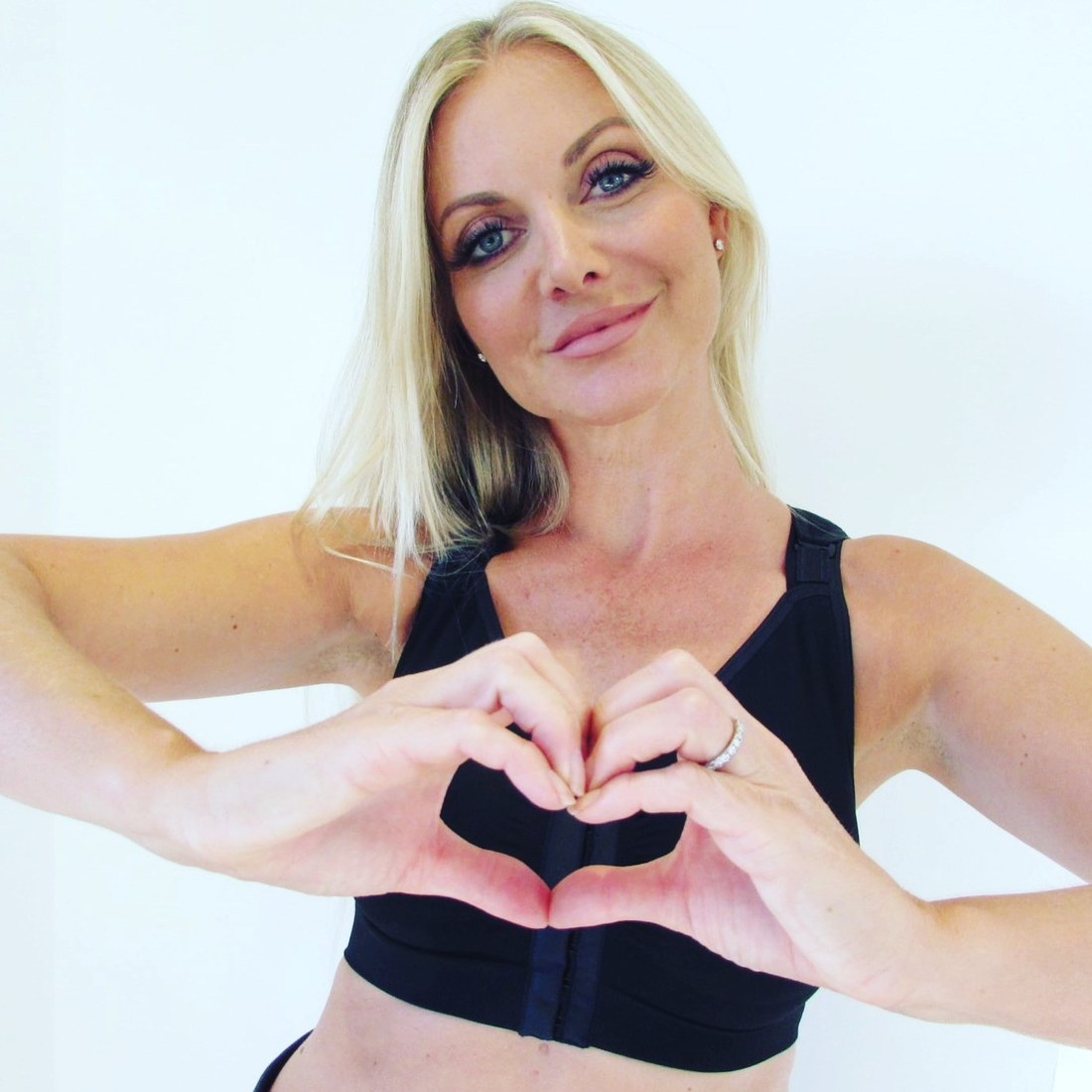 Woman wearing the black Reco Bra making a heart shape with her hands over the front fastening