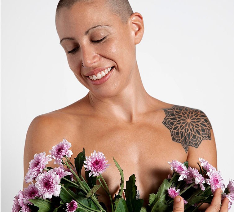 Woman with closely shaved hair smiling as she holds a bunch of pink chrysanthemums